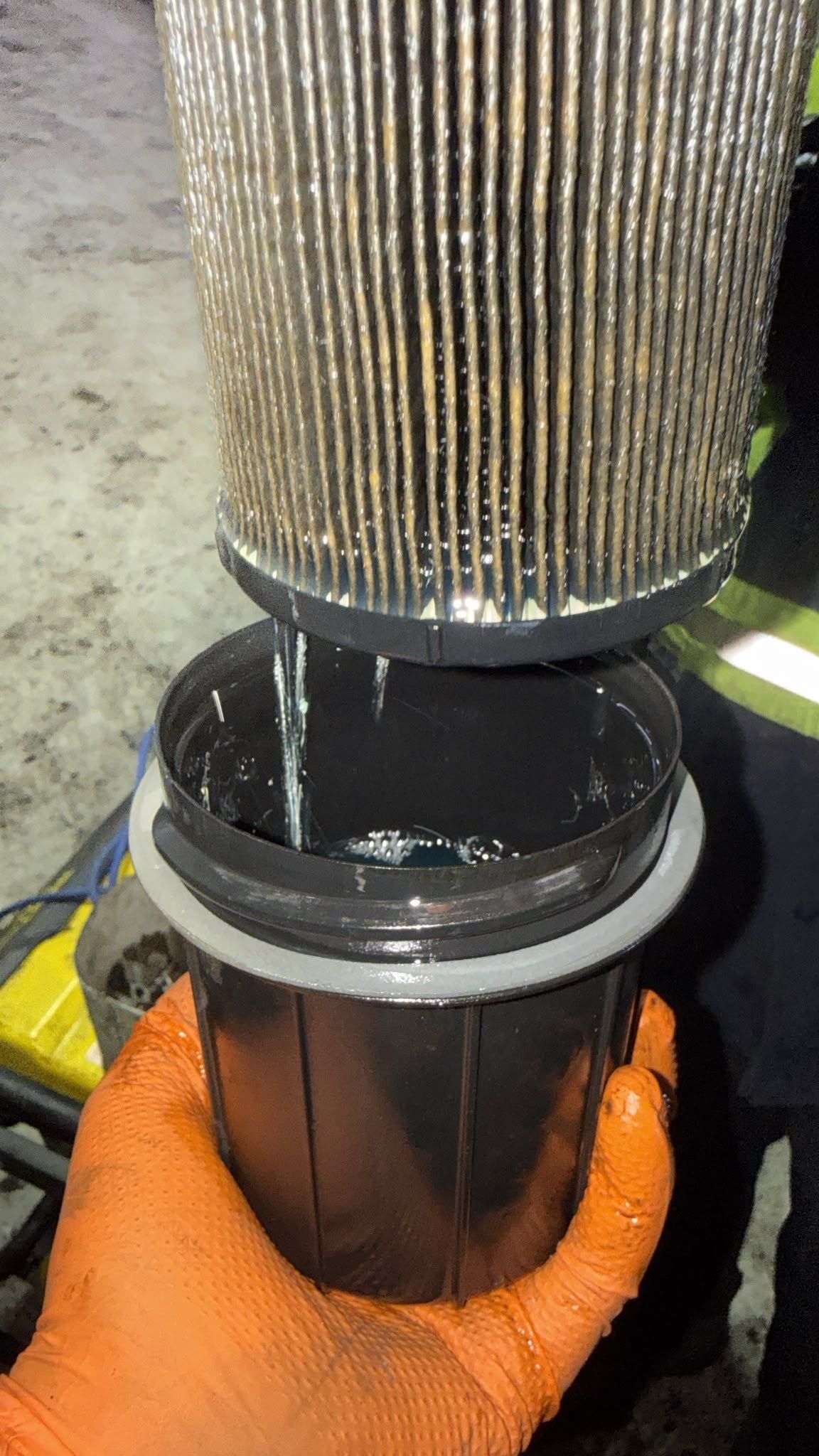 Gloved hand holding a fuel filter housing during a filter change